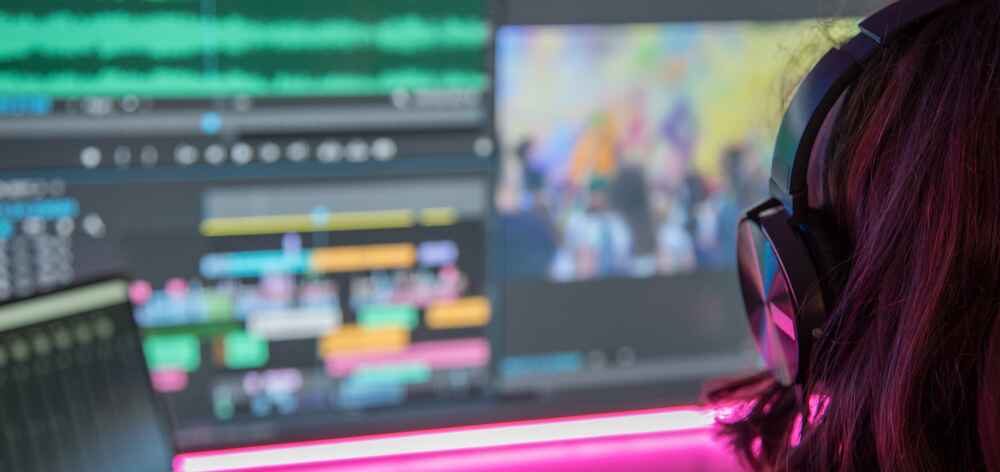 An over the shoulder shot of a woman editing videos on a computer screen.