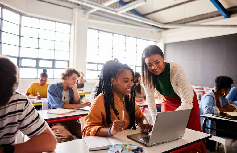 Photo of a female instructor assisting a female student on her laptop in a classroom setting