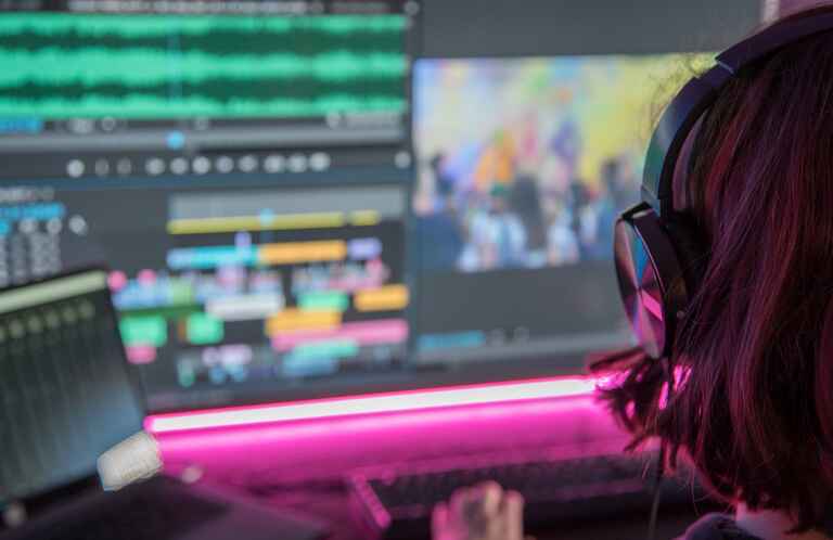 An over the shoulder shot of a woman editing videos on a computer screen.