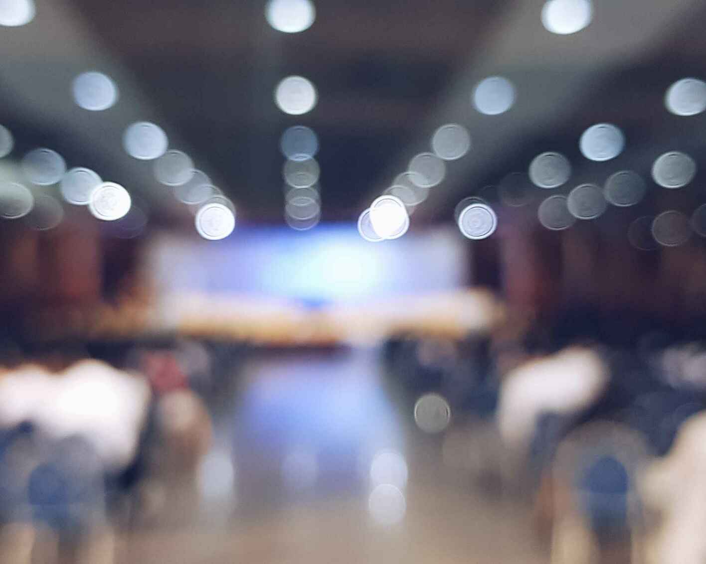 Blurred image of a large room filled with chairs facing a stage.