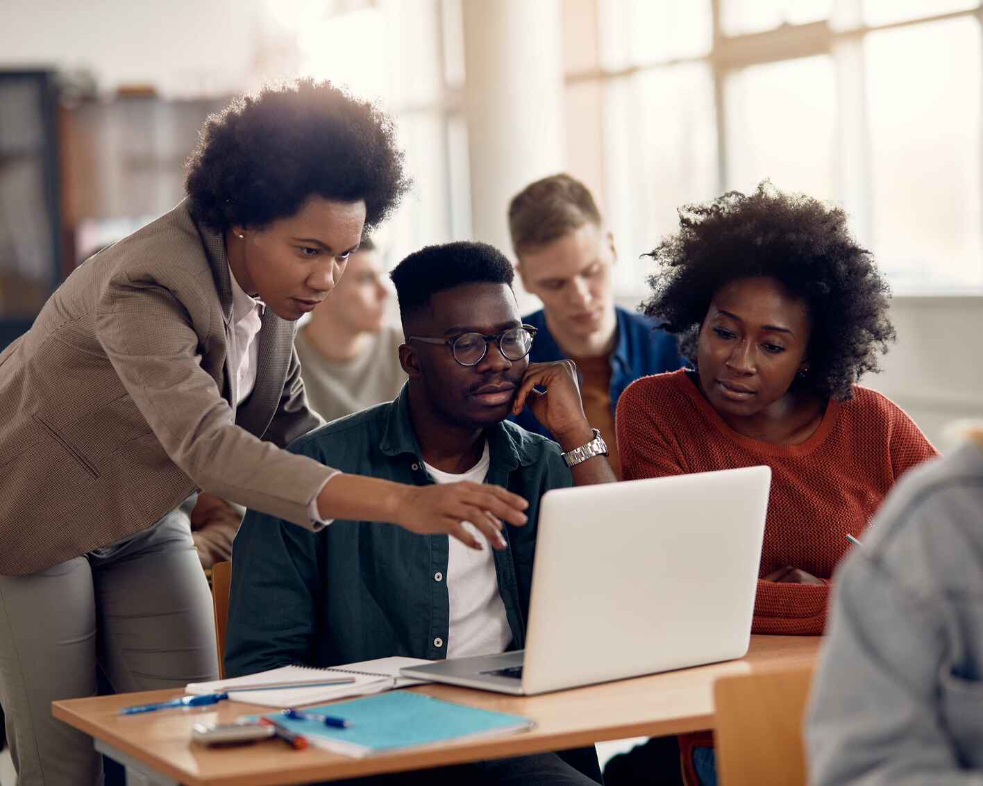 A teacher working with students, pointing to a student's laptop