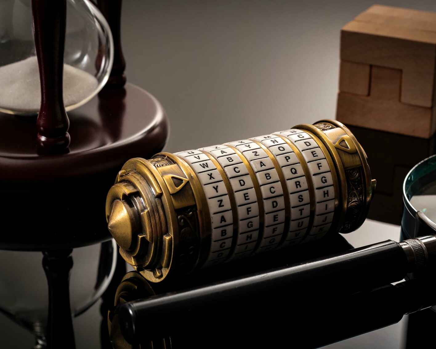 A close-up photograph of a cryptex, an hourglass, and a magnifying glass