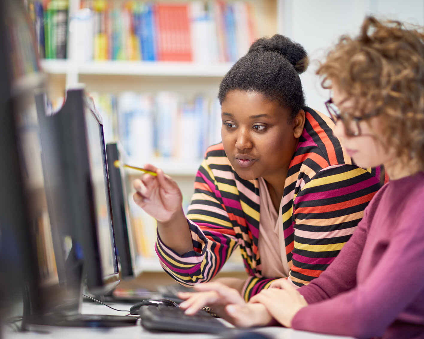 a female instructor guides a student while they both look on to a computer screen