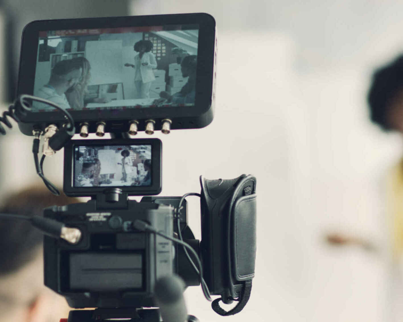 Person filming with video equipment, woman in background
