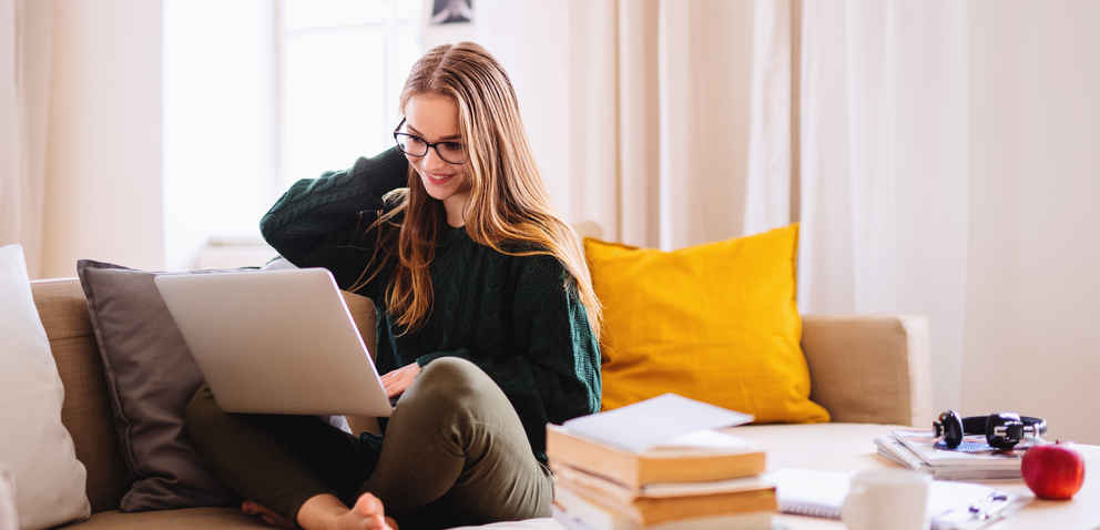 A young female student sitting on sofa, using laptop when studying