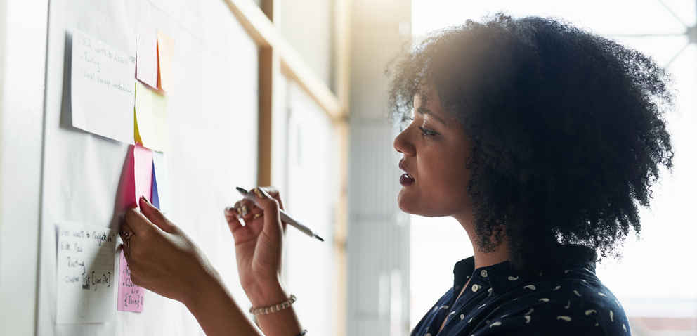 Woman of color writing on sticky notes stuck to a whiteboard