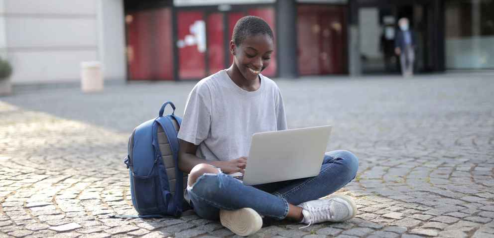 african american woman sitting on the ground smiling at her laptop