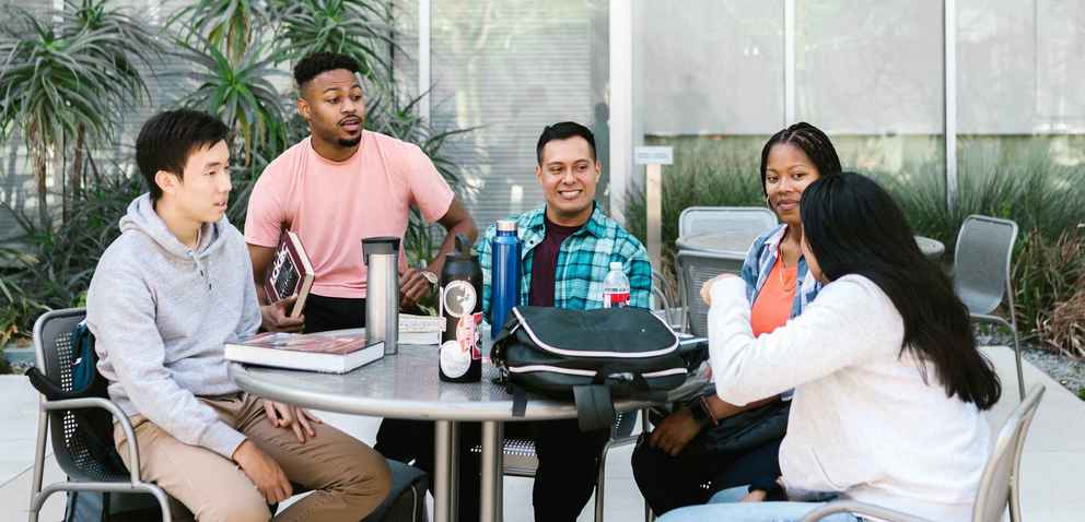 group of diverse students sit outside at a table having a discussion
