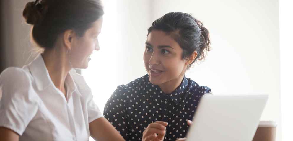 Two women talking while looking at a laptop computer
