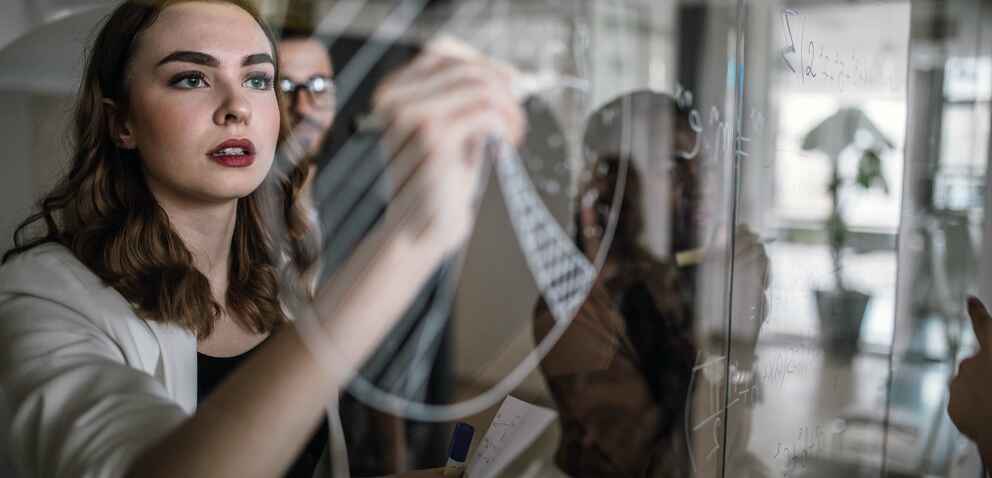 Photo of a woman drawing a pie chart on a clear transparent writing surface