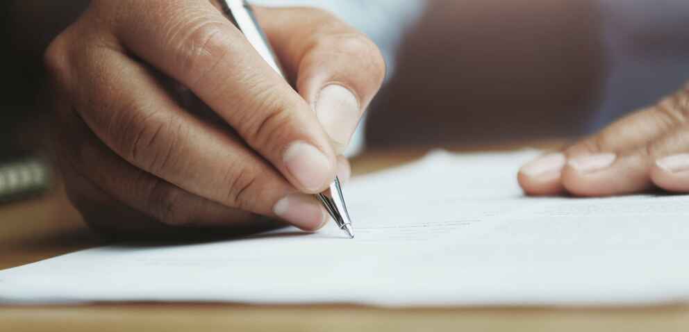 Photo of a man's hands holding a pen and writing on paper