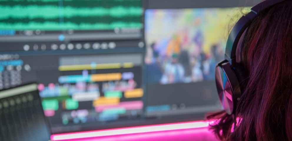 An over the shoulder shot of a woman editing videos on a computer screen.