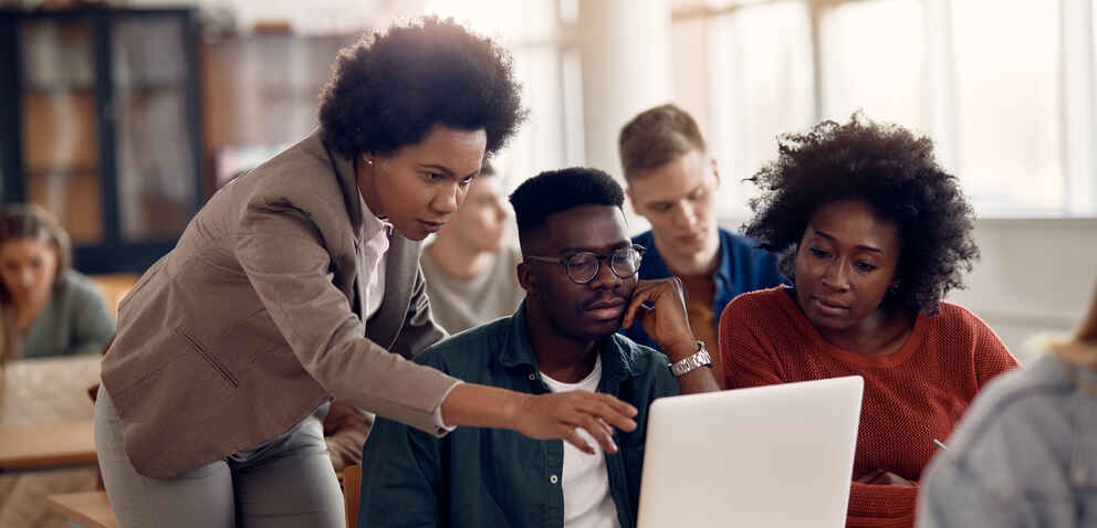 a female instructor guides two students looking at a laptop screen