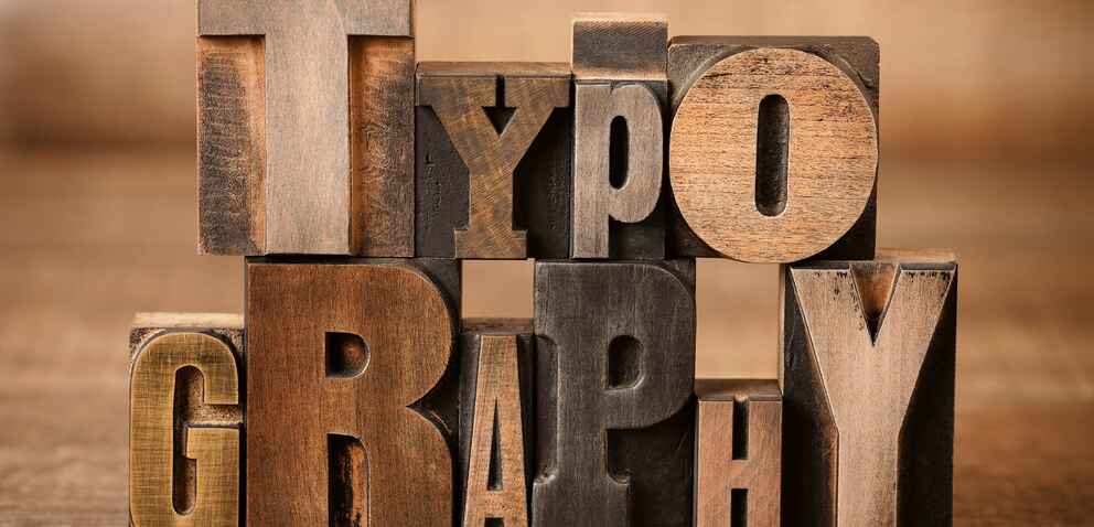 A stack of vintage wooden printing blocks arranged to spell “TYPOGRAPHY” in different fonts and sizes, creating a rustic and artistic visual effect.