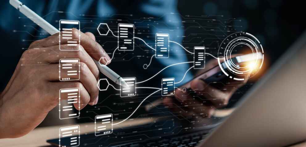 A person using a stylus and a smartphone, interacting with a laptop displaying interconnected digital documents and data flow, symbolizing digital document management.