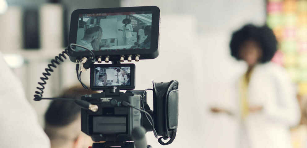 Person filming with video equipment, woman in background